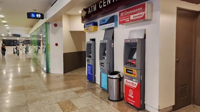 A row of three ATMs, one PNB and one Chinabank/BancNet, is located along a tiled indoor corridor labeled 'ATM Center' in a mall, Alabang Town Center, with people walking in the background