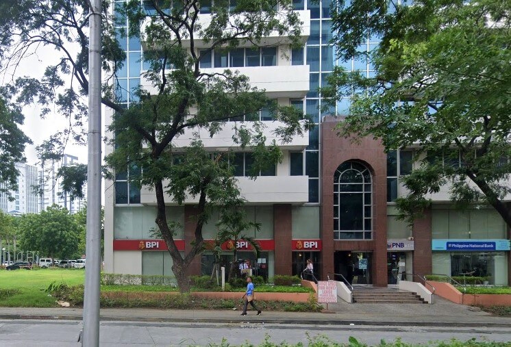 A ground-level view of a multi-story glass and concrete building with the BPI (Bank of the Philippine Islands) and PNB (Philippine National Bank) logos visible on the lower commercial level