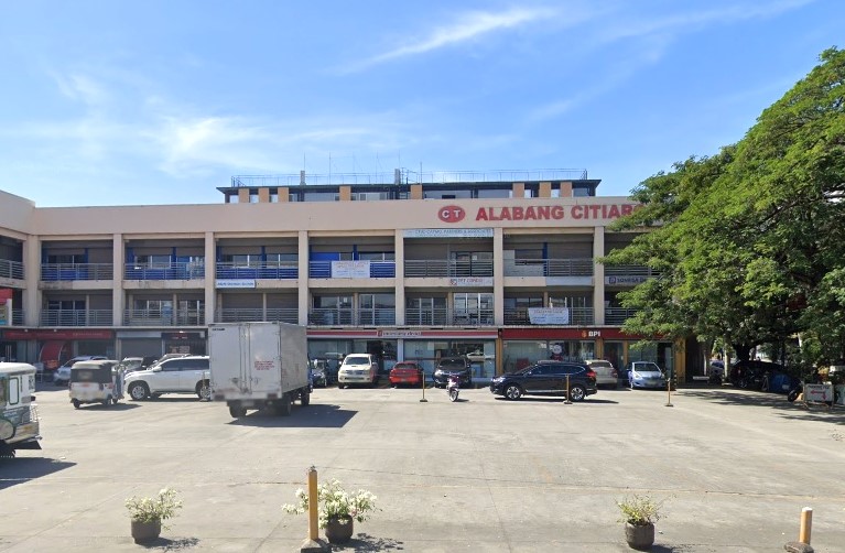 A wide, three-story commercial building complex, labeled "ALABANG CITIARCADE" in red text on the upper-floor facade. The lower floor features several storefronts, including the red-and-white sign for a BPI bank branch visible on the far right