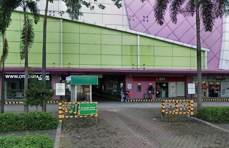 his photo of the entrance to a commercial building shows the BPI Alabang South Branch on the ground floor. The facade of the building above is bright green and pink. There is a sloping paved driveway leading to a covered area