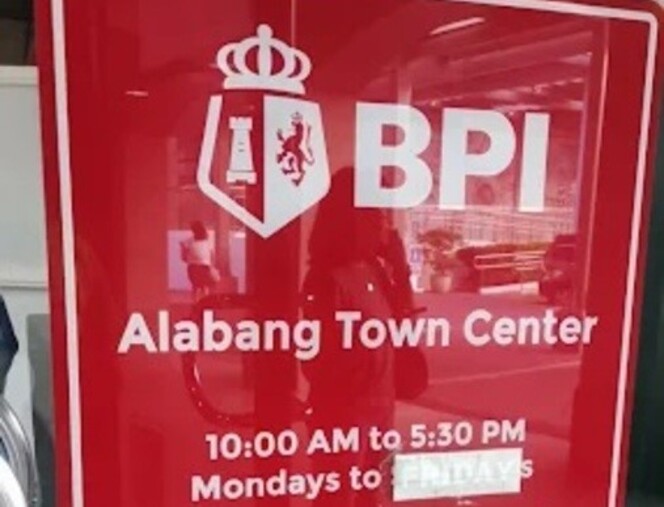 A red BPI bank sign on a glass door identifying the BPI Alabang Town Center branch. The sign lists operating hours as 10:00 AM to 5:30 PM, Mondays to FRIDAYS, with a white sticker partially obscuring the word "FRIDAYS"