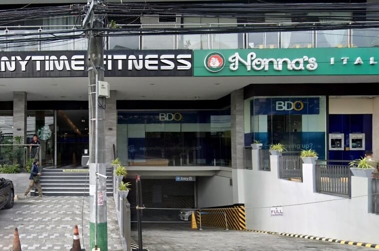 Exterior view of a multi-story commercial building featuring the signs for BDO Bank, Anytime Fitness, and Nonna's Italian restaurant, with a covered parking entrance in the center.