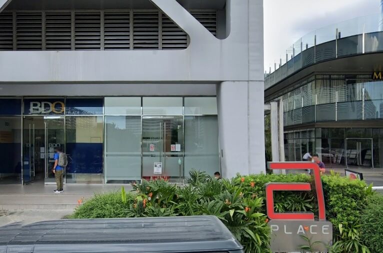Exterior of the BDO bank branch entrance, marked 'BDO A Place - Coral Way' on a modern, light-colored building, with green foliage in the foreground and a red 'A PLACE' sign on the right