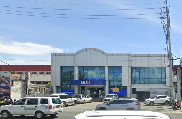 Exterior photo of BDO A. Santos – St. James Branch, a modern two-story building with blue signage, light gray metallic panels, and large blue tinted windows, with several cars parked in front