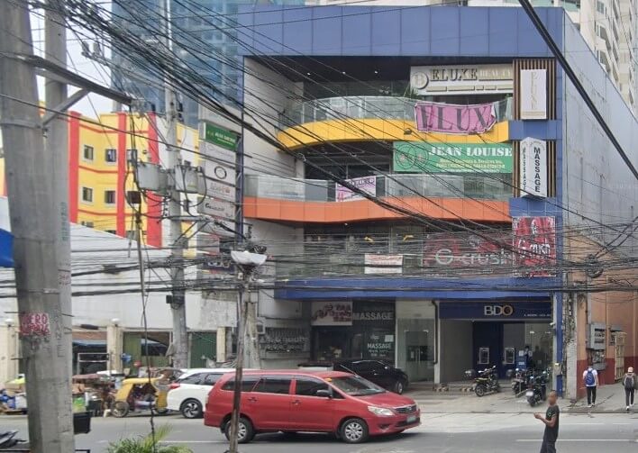 An outdoor photo of a multi-story commercial building with a BDO bank branch on the ground floor. The building has bright blue, orange, and yellow accents. Numerous tangled utility lines and electrical wires are prominent in the foreground
