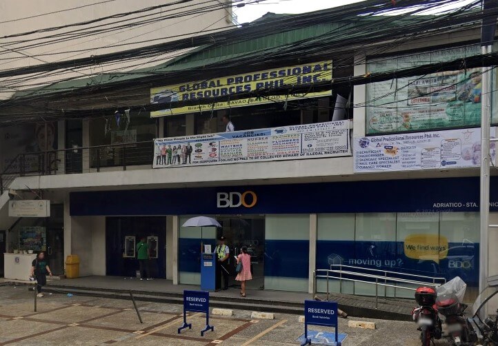 Exterior street-level view of a BDO bank branch (Adriatico - Sta. Monica) with a large blue sign. Above the bank, a second floor features signage for 'Global Professional Resources Phil. Inc.' and other services. Cluttered utility wires hang overhead