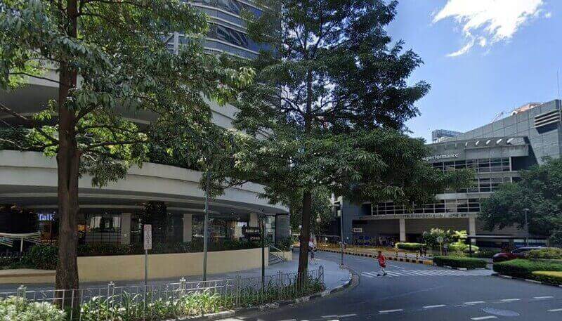 Street view of the BPI Ayala North Exchange office building in Makati, featuring a curved modern facade, lush green trees, and a pedestrian crosswalk