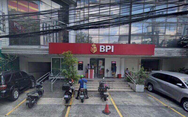 The exterior of a BPI (Bank of the Philippine Islands) branch featuring a red sign and logo, with a ramp, an ATM, and several motorcycles parked in front