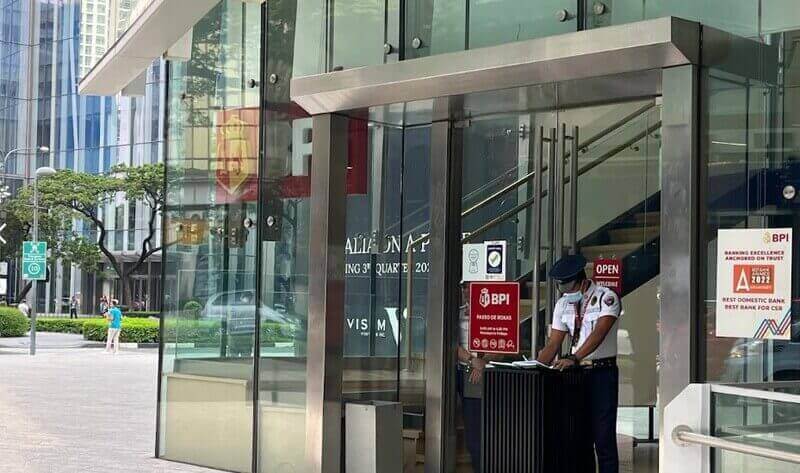 Exterior entrance of the BPI Paseo de Roxas branch in Makati, featuring a modern glass facade, a security guard at a podium, and signage for the bank’s 2022 awards