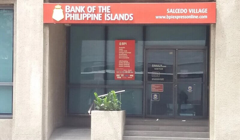 Exterior entrance of a Bank of the Philippine Islands (BPI) branch in Salcedo Village, featuring a red storefront sign with the bank’s logo and website