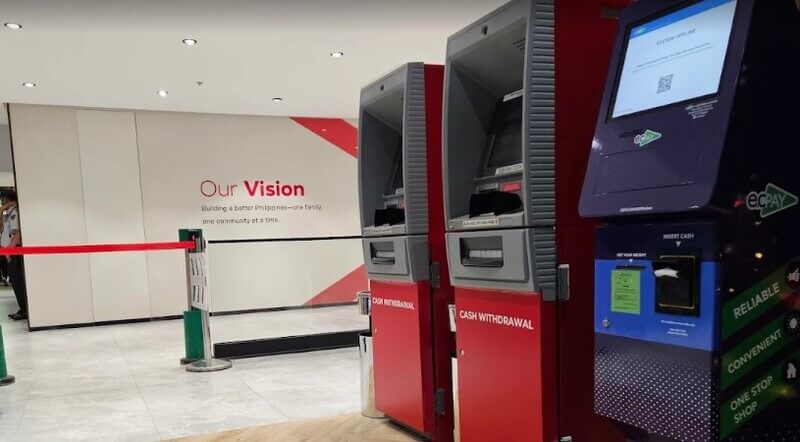 Row of red BPI cash withdrawal ATMs and a blue ECPay kiosk inside a modern bank branch, with a wall in the background displaying the text "Our Vision: Building a better Philippines."
