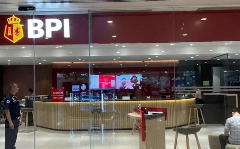 The modern storefront of a BPI branch at One Ayala, featuring the glowing red and gold logo above a glass-walled interior with a curved service counter and digital displays