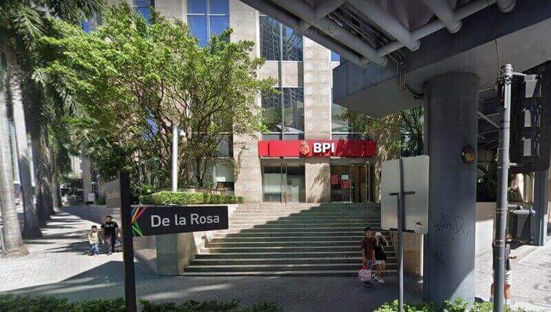Street-level view of the BPI branch at The Enterprise Center in Makati, showing the red bank signage, a "De la Rosa" street sign, and pedestrians on the sidewalk