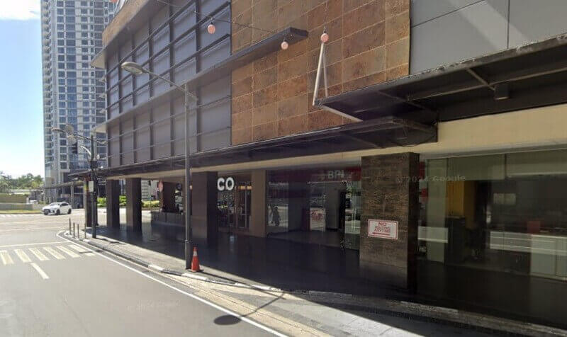 Exterior view of the BPI branch at Glorietta Mall, showing the ground-level storefront with large glass windows, a dark canopy, and a nearby crosswalk on a paved street