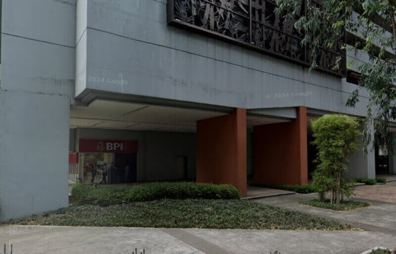 Exterior street-level view of a BPI (Bank of the Philippine Islands) branch located on the ground floor of The Columns Ayala Avenue building, featuring gray concrete walls, large brown pillars, and decorative metal screens