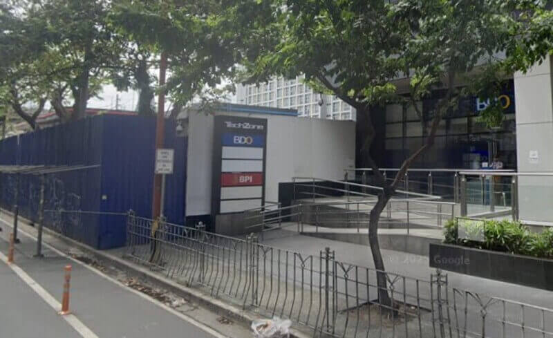 Street-level view of the TechZone building entrance in Makati, showing signage for BDO and BPI banks next to a pedestrian ramp and sidewalk