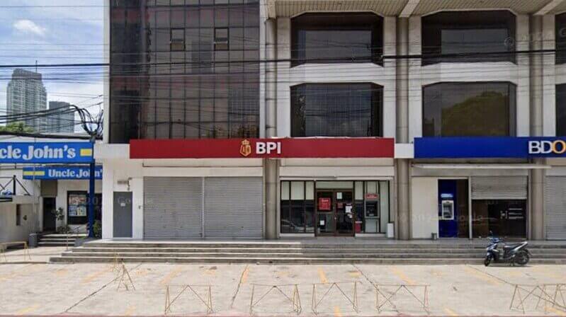 Street-level view of a commercial building storefront featuring a BPI branch Pasong Tamo La Fuerza with a red sign, flanked by an Uncle John's convenience store and a BDO bank branch