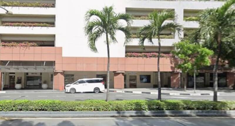 An exterior view of the BPI San Lorenzo branch located at Ayala Avenue Tower, showing a white car parked in front of the multi-story building with neatly arranged palm trees and greenery