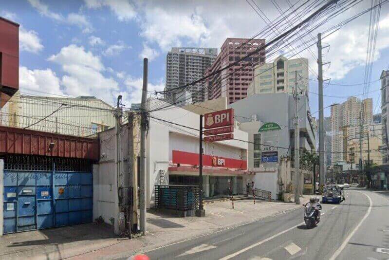 Exterior view of a BPI Vito Cruz Chino Roces branch located at the corner of Vito Cruz and Chino Roces Avenue, featuring the red and white corporate signage, street-level entrance, and surrounding urban buildings under a blue sky