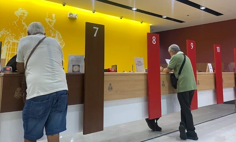 Interior of a BPI Ayala Malls Circuit branch featuring customers at teller counters numbered 7 through 10, with a vibrant yellow and red wall design and wood-finish counters