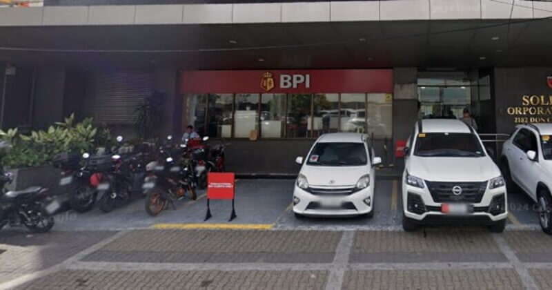 Street-level view of a BPI (Bank of the Philippine Islands) branch office at Pasong Tamo, featuring the red and gold storefront logo, a parking area with cars and motorcycles, and the building entrance
