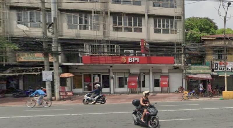 Street-level view of the BPI Balut Tondo branch featuring a red storefront, passing motorcycles, and overhead power lines