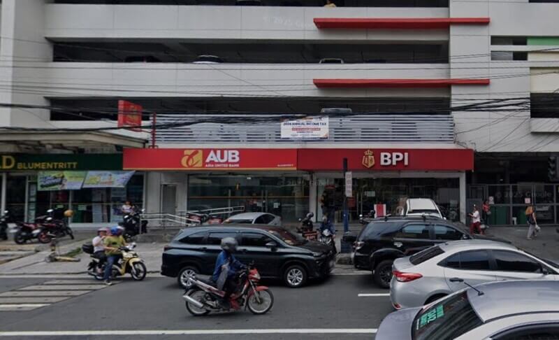 Exterior view of the BPI and AUB bank branches situated side-by-side on the ground floor of a multi-story building, with a busy street and vehicles in the foreground