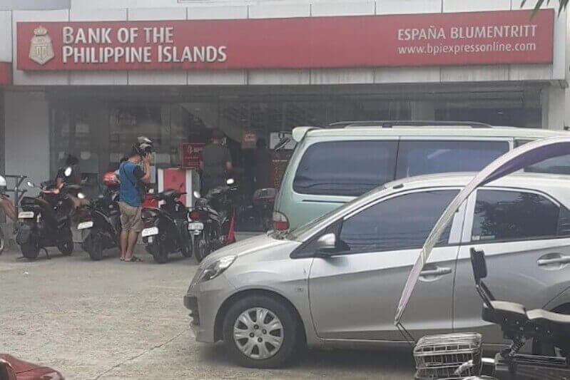 Exterior view of the Bank of the Philippine Islands (BPI) España Blumentritt branch, featuring the bank's signage above the entrance, with several parked cars and motorcycles in the foreground
