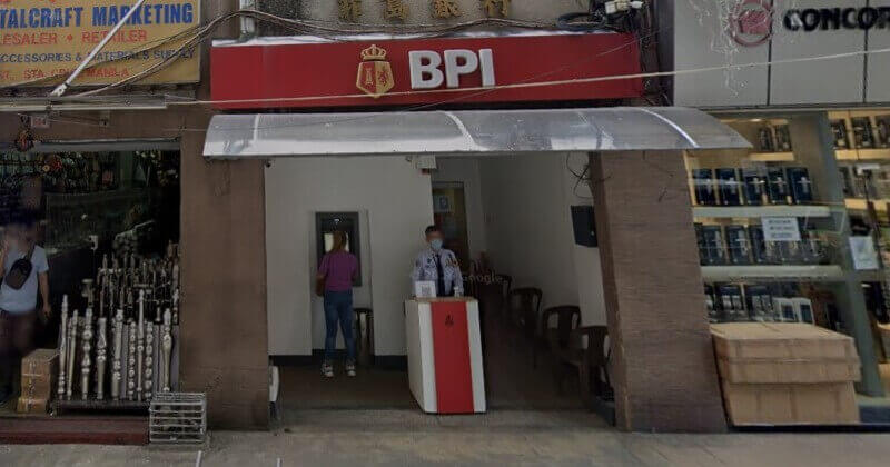 Exterior view of a BPI branch T.Alonzo entrance featuring a red sign with the gold crest logo, a security guard standing at a podium, and a customer using an ATM
