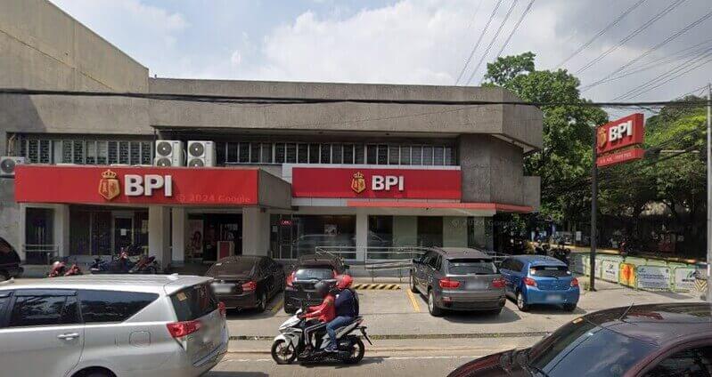 Exterior view of a BPI (Bank of the Philippine Islands) branch located at UN Avenue, Pope Pius Center, featuring the red corporate signage, a concrete building facade, and several cars parked in front