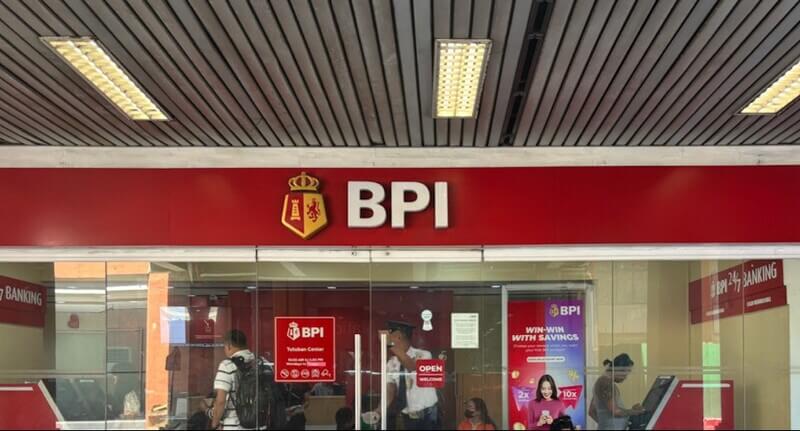 The storefront of a BPI (Bank of the Philippine Islands) Tutuban Center branch, featuring its red signage, shield logo, and glass entrance where customers and a security guard are visible