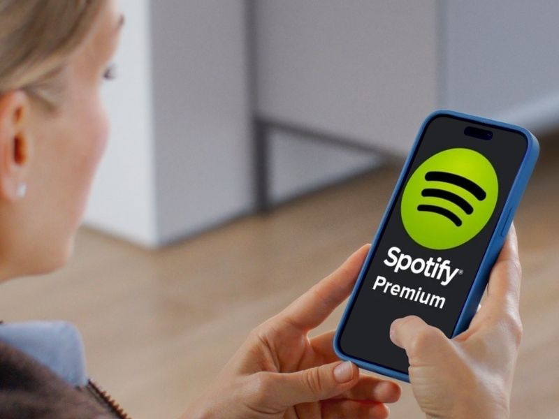 Close-up over-the-shoulder view of a person holding a smartphone displaying the Spotify Premium logo on the screen